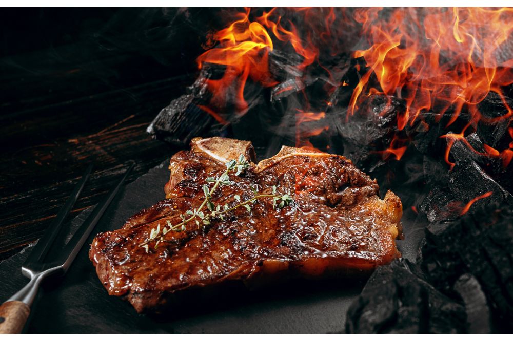 barbeque steak on a black slate board with meat fork and grill coals