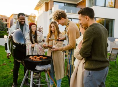 White man grilling meat during barbeque with his friends on backyard